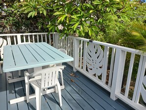 Ein blauer Tisch im Freien mit weißen Stühlen auf einer Holzterrasse mit weißen Geländern.