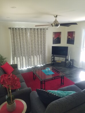 Ein Wohnzimmer mit einer Couch, einem Couchtisch, einem Fernseher und einem Deckenventilator.