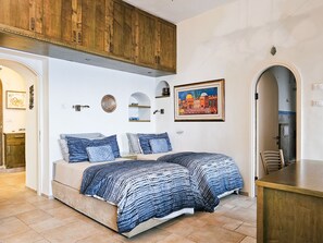 Quarto com cama, armários de madeira, um quadro e um banheiro visível através de um arco.