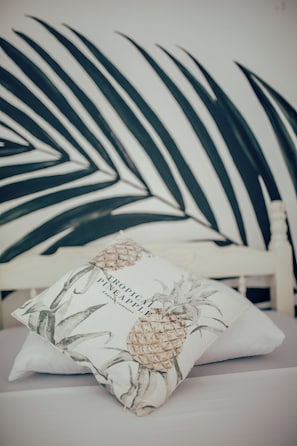 Een kussen met een ontwerp van ananas en palmblad, op een bed met een wit hoofdeinde.