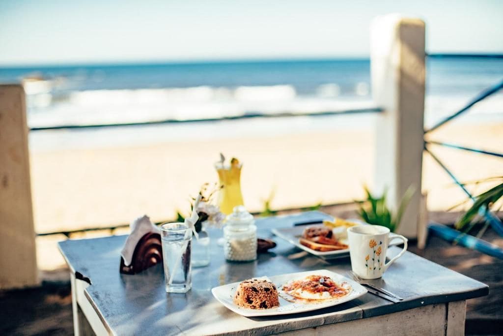 Ein Tisch mit Essen, einem Glas Wasser und einer Tasse vor einer Strandkulisse.