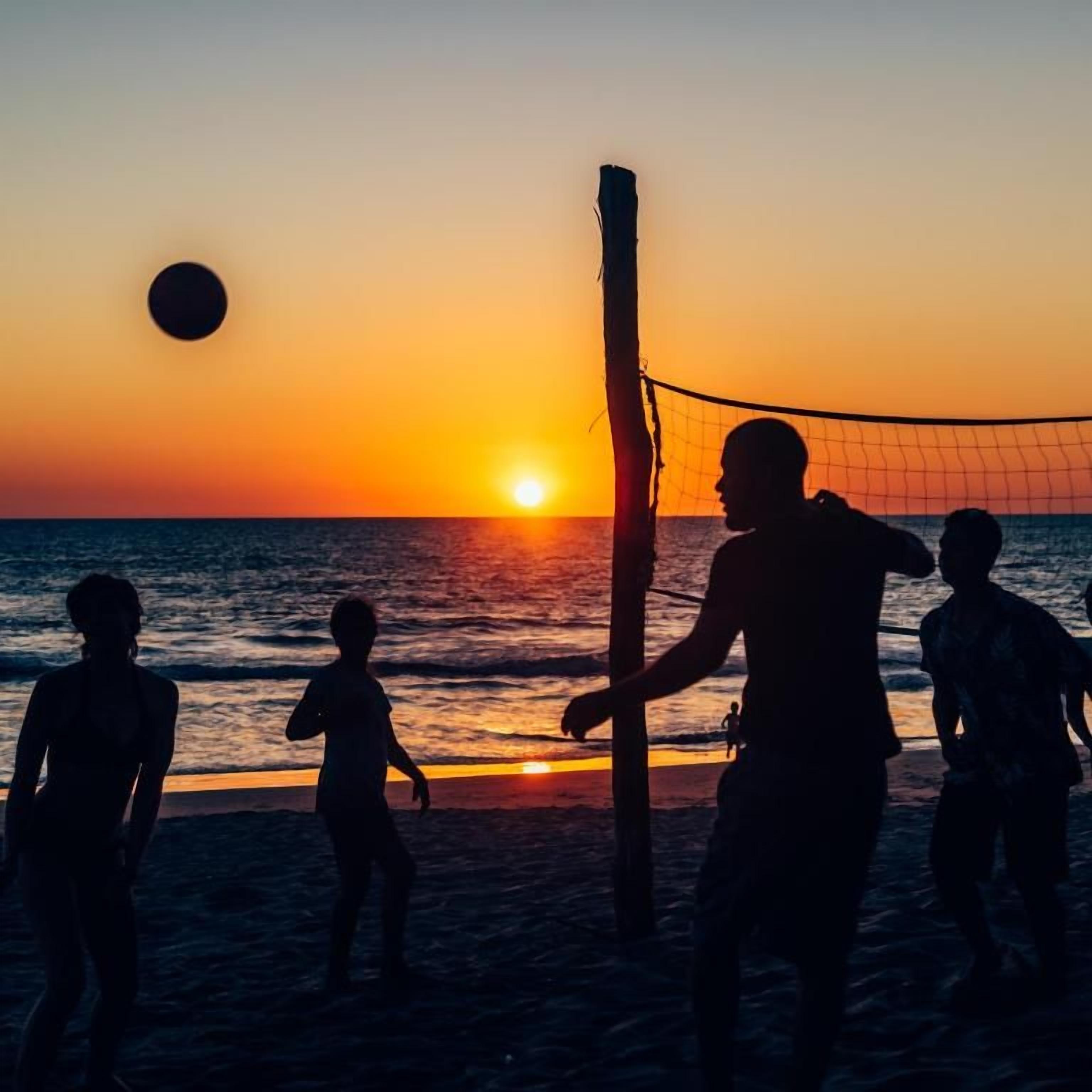 Silhouettes of people playing volleyball on a beach at sunset.