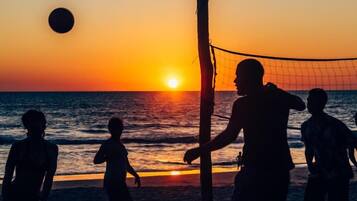 Silhouettes of people playing volleyball on a beach at sunset.
