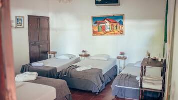A room with three beds, a ceiling fan, an air conditioning unit, a painting on the wall, and a wooden shelf with towels.