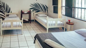 A room with two single beds, a small table, a window with curtains, and a wall with a leaf pattern. - Casita de Playa Bomalu (Las Peñitas)