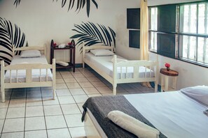 A room with two single beds, a small table, a window with curtains, and a wall with a leaf pattern. - Casita de Playa Bomalu (Las Peñitas)