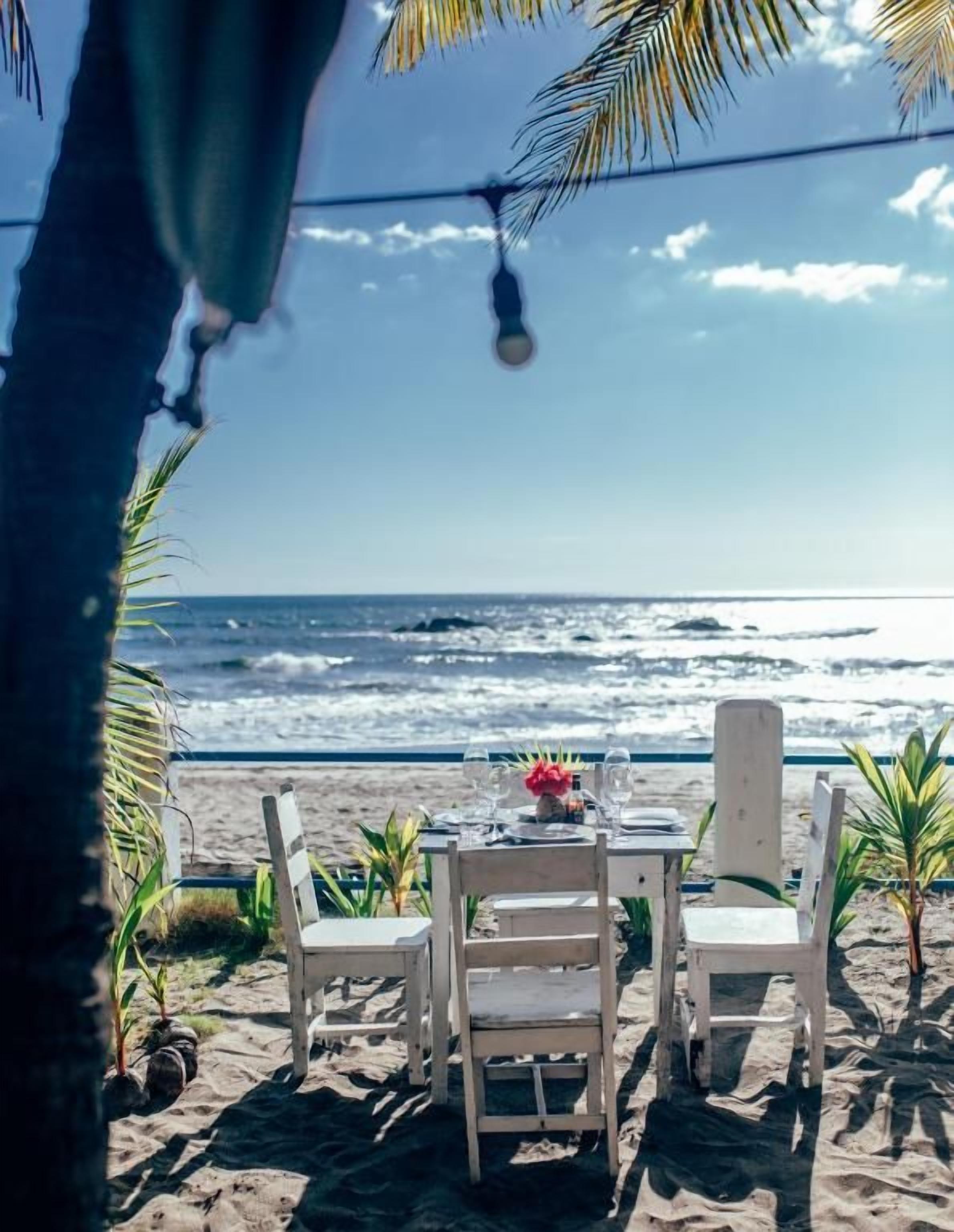 A beachside table with chairs and a table setting, overlooking the ocean.