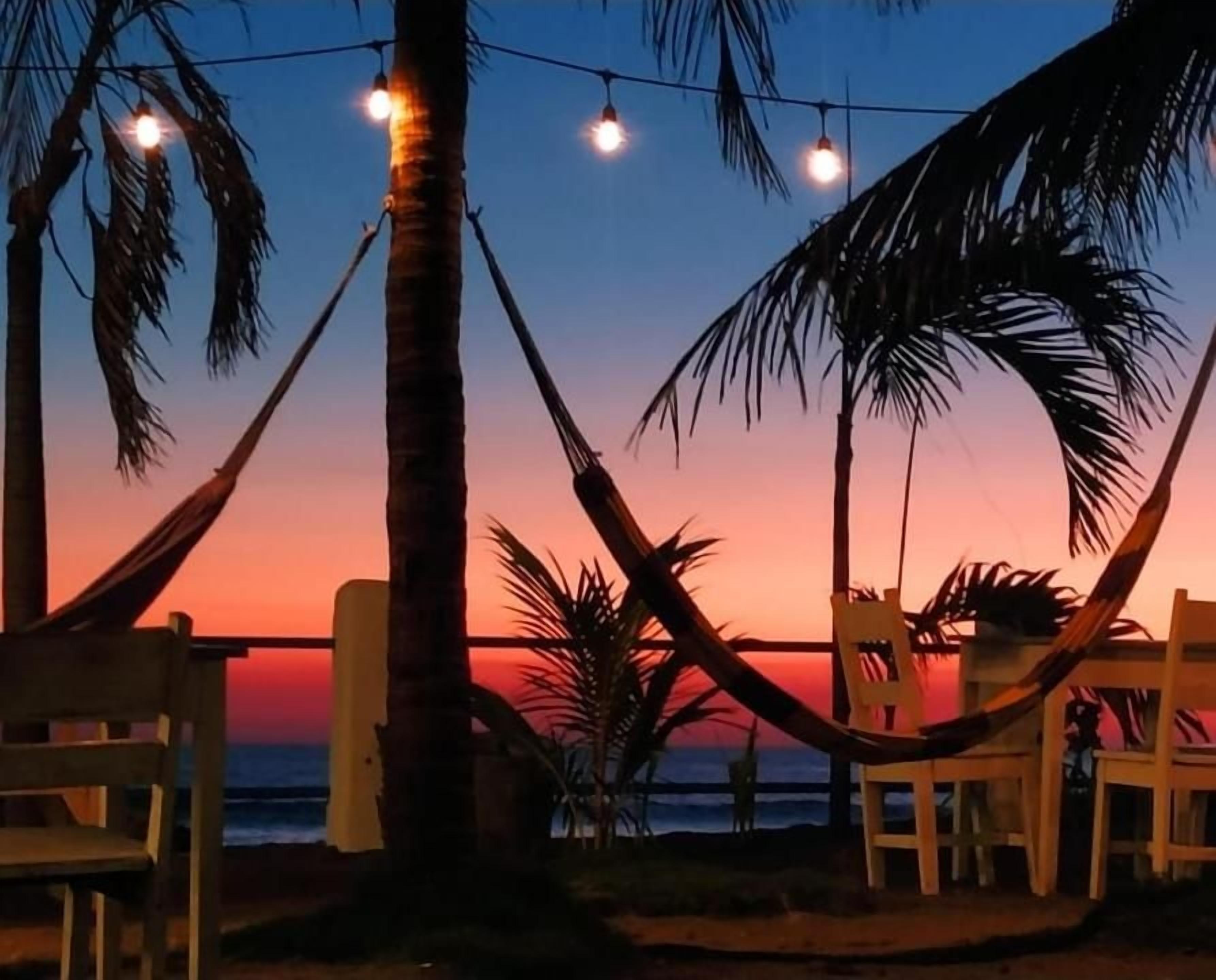 A beach setting with a hammock, chairs, and string lights.