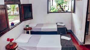 A room with two beds, a small table with a vase, and a window with a view of greenery. - Casita de Playa Bomalu (Las Peñitas)