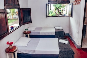 A room with two beds, a small table with a vase, and a window with a view of greenery. - Casita de Playa Bomalu (Las Peñitas)
