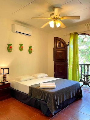 A bedroom with a bed, a ceiling fan, an air conditioning unit, and a view of the outdoors through a window with curtains. - Nambí Lodge (Las Peñitas)