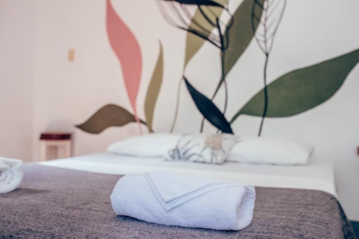 A neatly made bed with a folded towel and a pillow with a floral pattern.