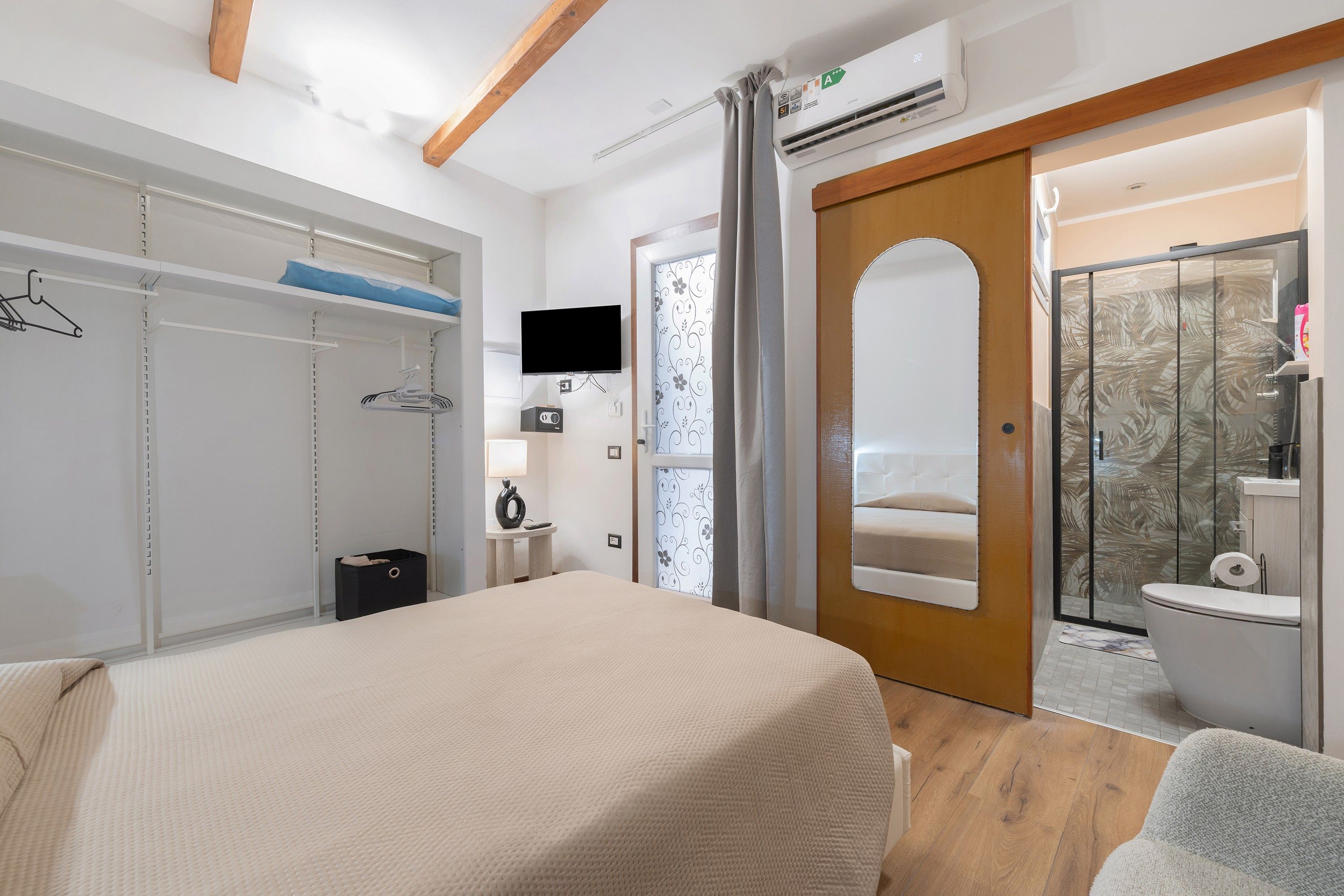 Et hotelværelse med seng, garderobeskab, fjernsyn og bruseområde.