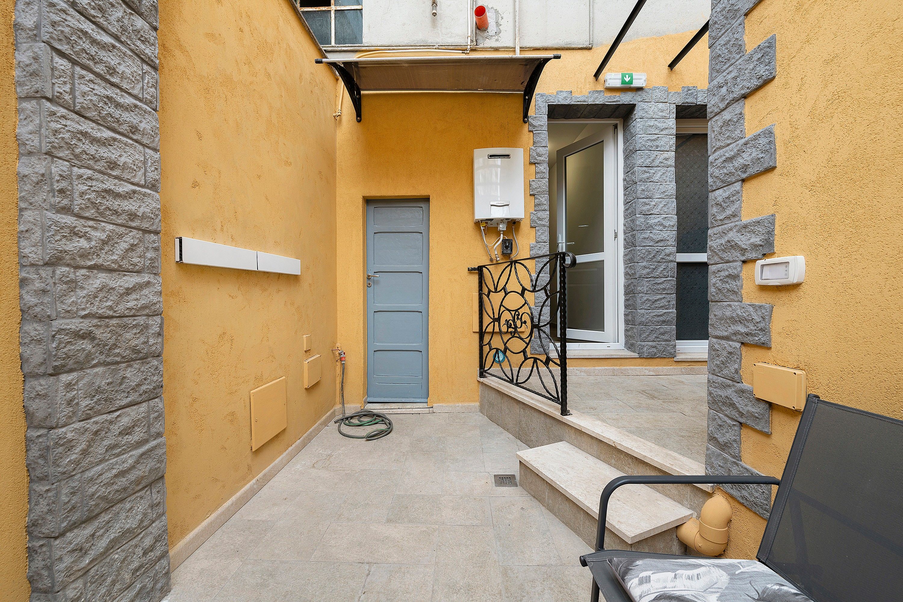 A narrow outdoor corridor with a blue door, a water heater, and a small bench.