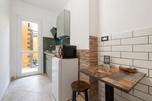 A compact kitchen with a refrigerator, microwave, and a small bar stool. - Empathy House – Room 1 (Cagliari)