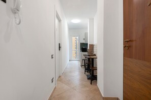 A hallway with a telephone, a door, and a kitchen area with a table and stools. - Empathy House – Room 2 (Cagliari)