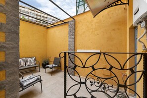 Une terrasse extérieure aux murs jaunes, dotée d’une rambarde en métal, d’un banc et d’une chaise.