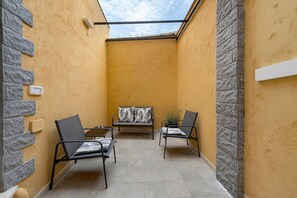 A small, enclosed patio area with a yellow wall, a skylight, and two chairs with cushions. - Empathy House – Room 3 (Cagliari)
