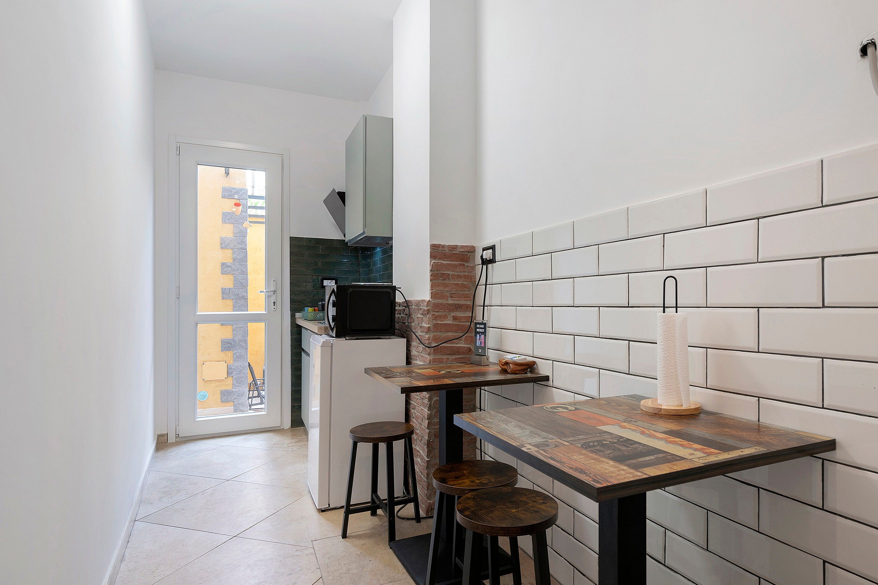 A narrow kitchen with a tiled backsplash, a refrigerator, a microwave, and a small bar area with stools.