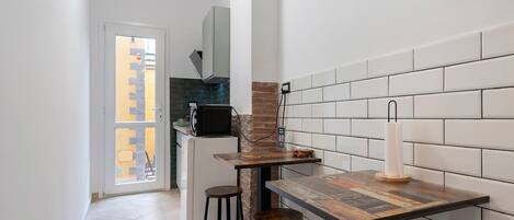 A narrow kitchen with a tiled backsplash, a refrigerator, a microwave, and a small bar area with stools.