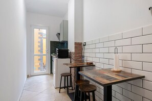 Une cuisine étroite avec un mur recouvert de carreaux, un réfrigérateur, un four à micro-ondes et un petit coin bar avec des tabourets.