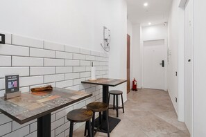 A narrow hallway with a white tiled wall, a wooden door, and a fire extinguisher. - Empathy House – Room 3 (Cagliari)