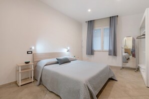 Une chambre à coucher comprenant un lit, des tables de chevet, une fenêtre avec des rideaux, un miroir et une armoire.