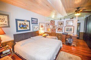 A hotel room with a large bed, a desk, and multiple framed pictures on the walls.