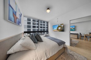 A modern bedroom with a large bed, a view of a cityscape through the window, and a flat-screen TV on the wall. - 225 Miami Building - We Host (Miami)