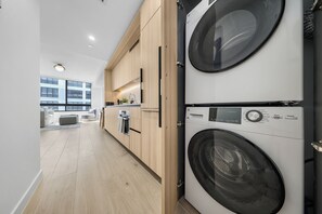 Ein moderner Waschraum mit zwei Waschmaschinen mit Frontlader, Holzschränken und Blick auf eine Stadtlandschaft durch große Fenster.