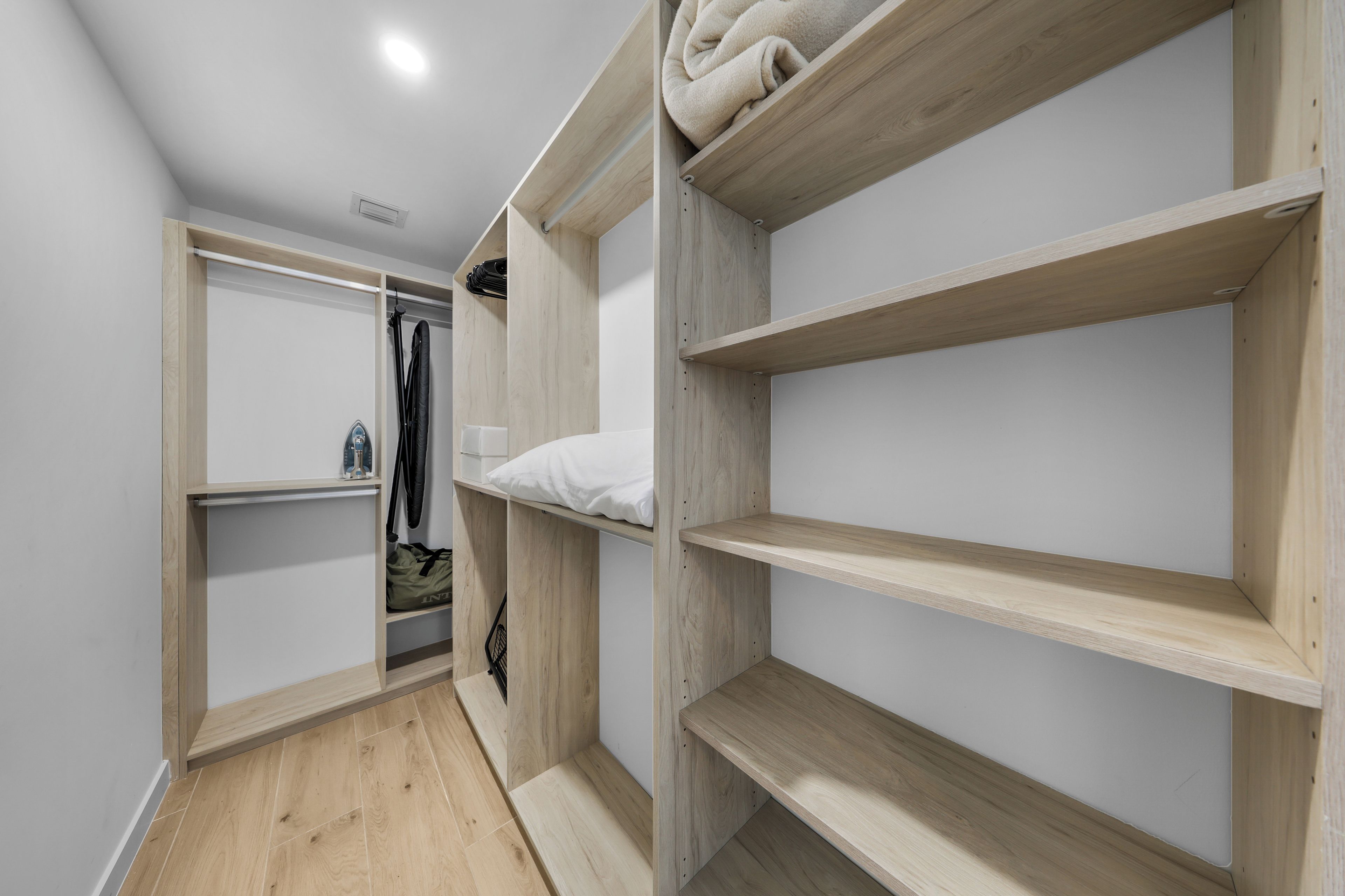 A modern, minimalist room with built-in wooden shelving units, a white closet with hanging space, and a wooden floor.