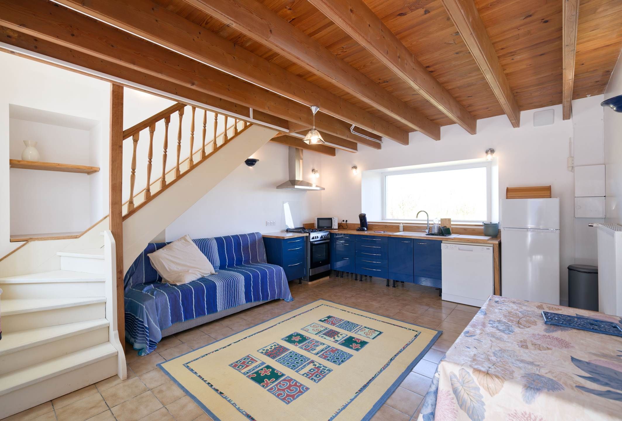 Eine moderne Küche mit blauen Schränken, einer Holztreppe und einem Essbereich mit Tisch und Stühlen.