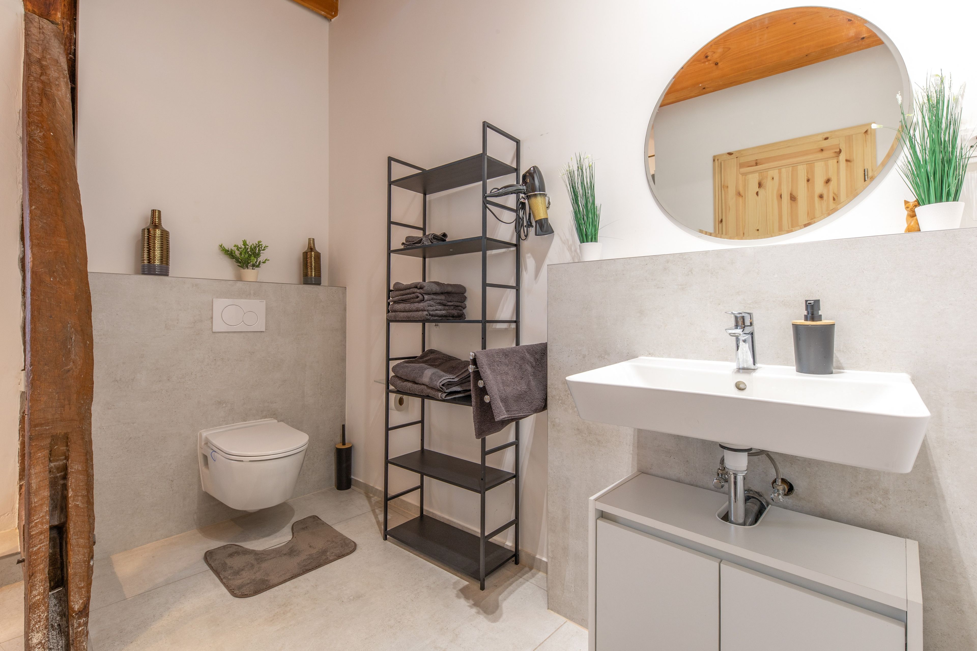 A bathroom with a white sink, a toilet, a towel rack, and a shelf unit.