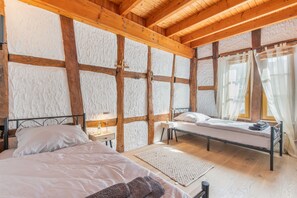 Et soveværelse med træloft, en seng med hvide sengetøj, et natbord med en lampe og et vindue med gardiner.