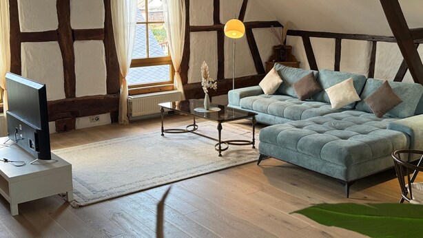 Une pièce confortable avec une grande fenêtre, un canapé, un téléviseur et une lampe.