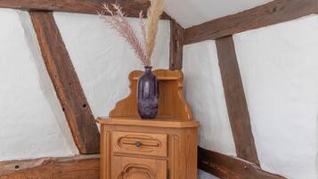 A wooden cabinet with a vase containing dried plants, set against a white wall with exposed wooden beams.