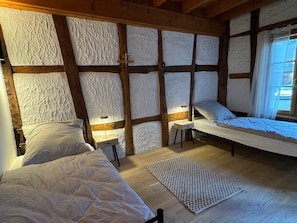 Ein Zimmer mit zwei Betten, einem kleinen Tisch und einem Fenster mit Vorhängen.
