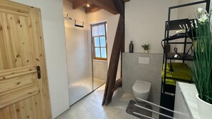 Une salle de bain avec une porte en bois, une douche, des toilettes et une étagère avec des plantes.