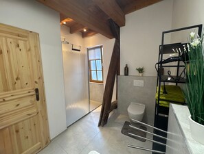 Ein Badezimmer mit Holztür, einer Dusche, einer Toilette und einem Regal mit Pflanzen.
