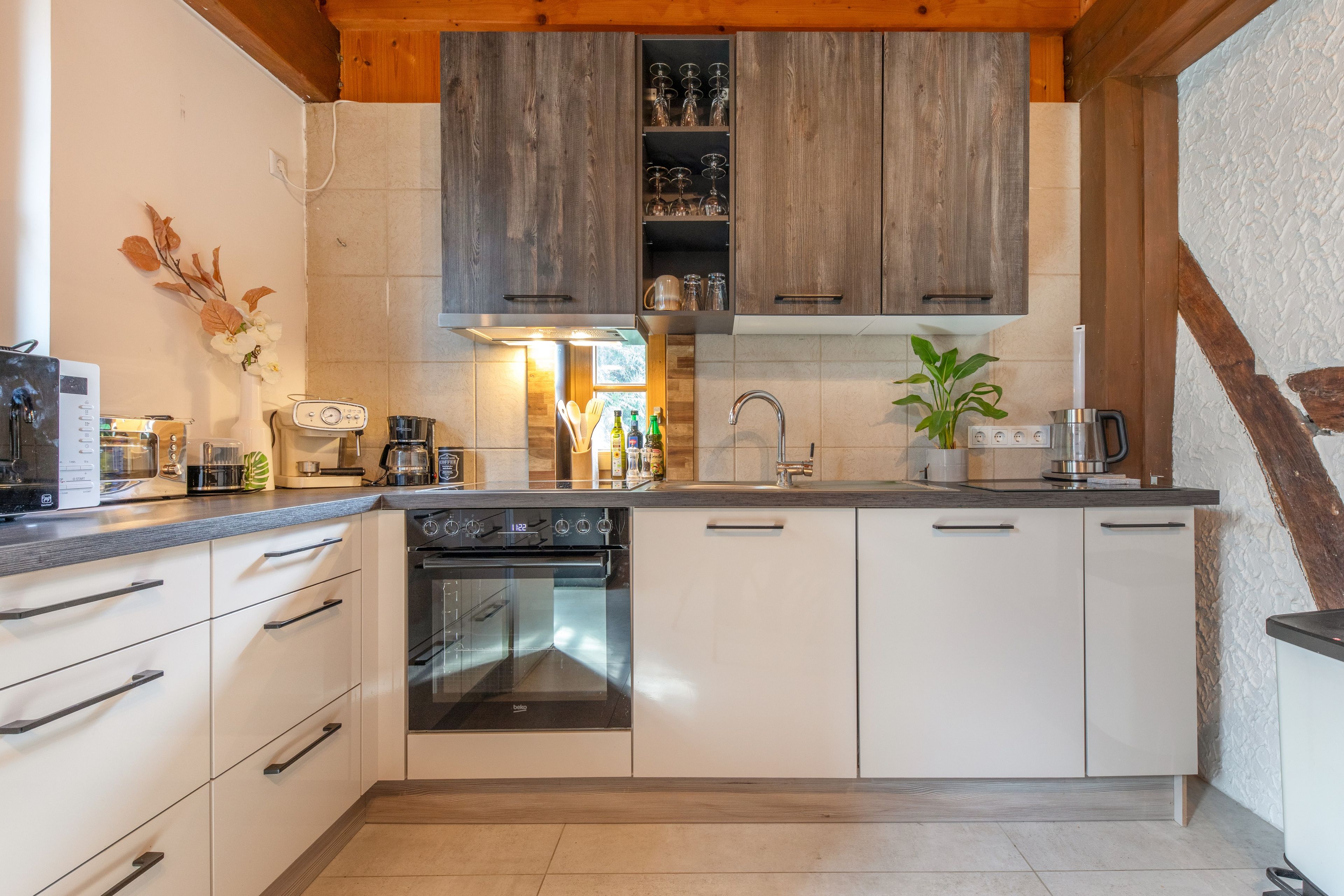 A modern kitchen with white cabinetry, a built-in oven, and a coffee machine.