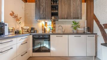 A modern kitchen with white cabinetry, a built-in oven, and a coffee machine.
