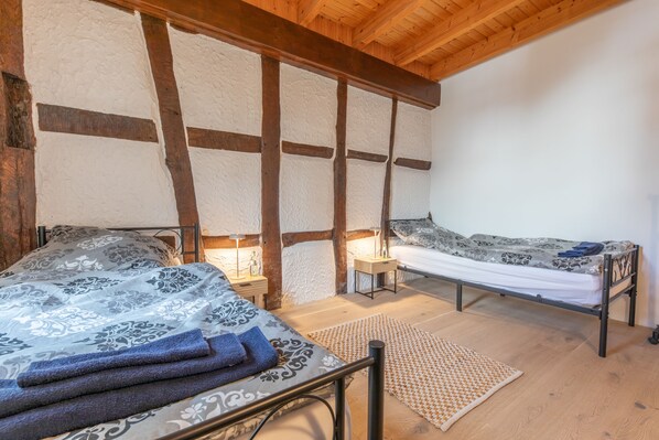 A room with two beds, a wooden ceiling, and a textured wall.