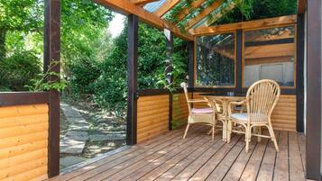 Une terrasse en bois avec une table et des chaises, entourée d’une clôture en bois et de verdure.