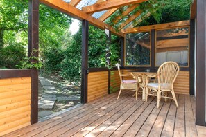 A wooden deck with a table and chairs, surrounded by a wooden fence and greenery.