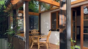 Une terrasse en bois avec une table et des chaises, entourée d’une clôture en bambou et de verdure.