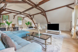 A spacious loft with exposed wooden beams, a large sectional sofa, a flat-screen TV, and a dining area with natural light. - Holiday Home 'Landhaus Auszeit' with Private Terrace, Private Garden and Wi-Fi (Braubach)
