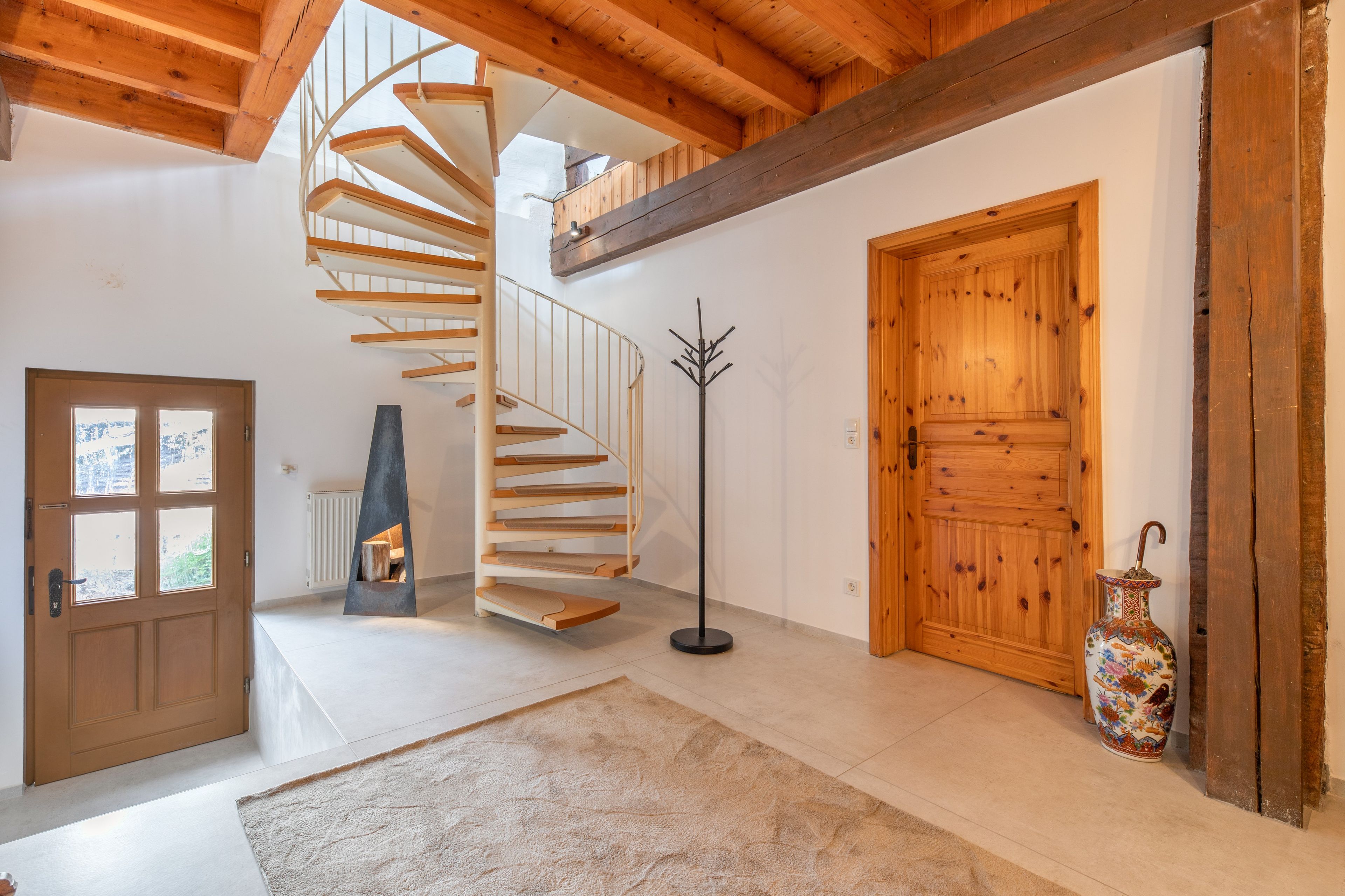 A spiral staircase with a wooden finish, a large wooden door, and a decorative vase.