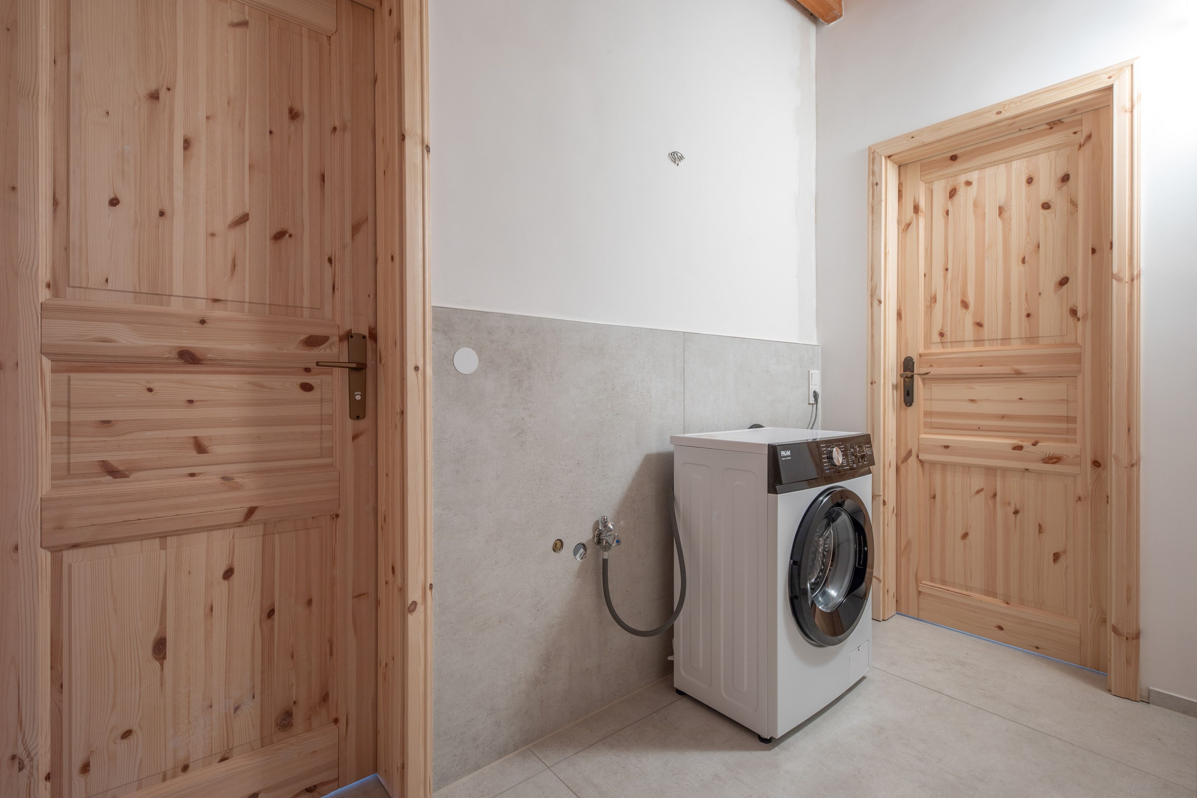 Ein Waschraum mit Holztüren, einer Waschmaschine und einer gefliesten Wand.