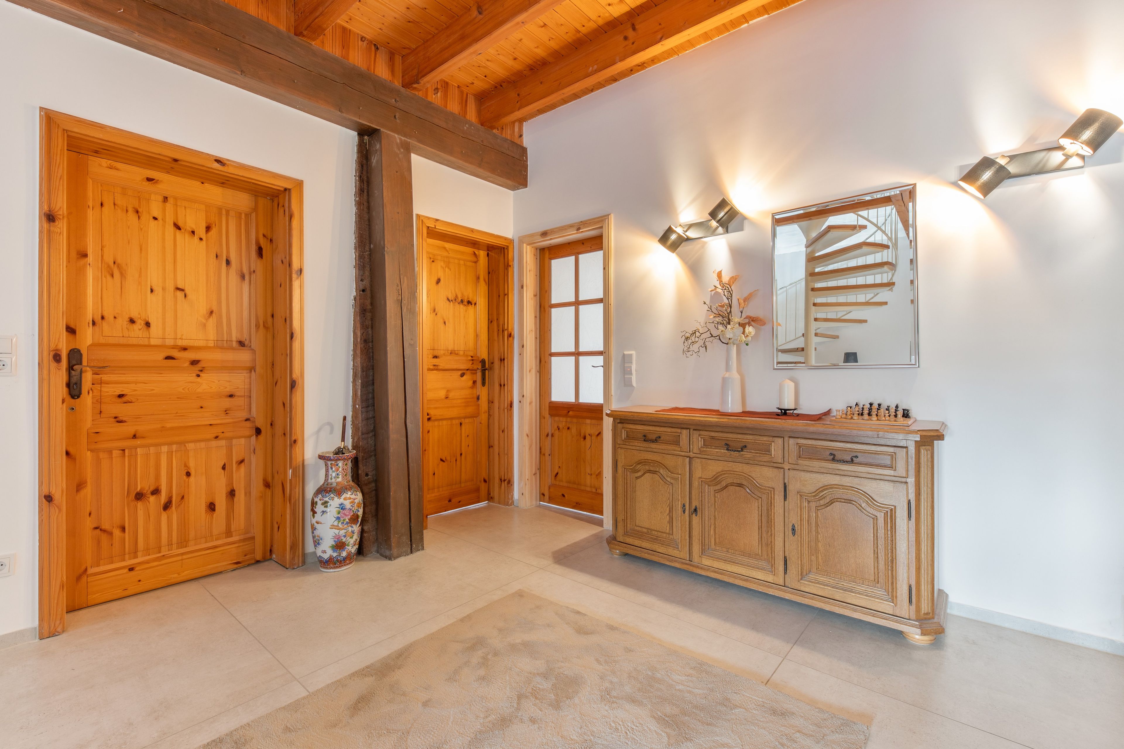 Un couloir avec des portes en bois, un miroir, une armoire et un vase.