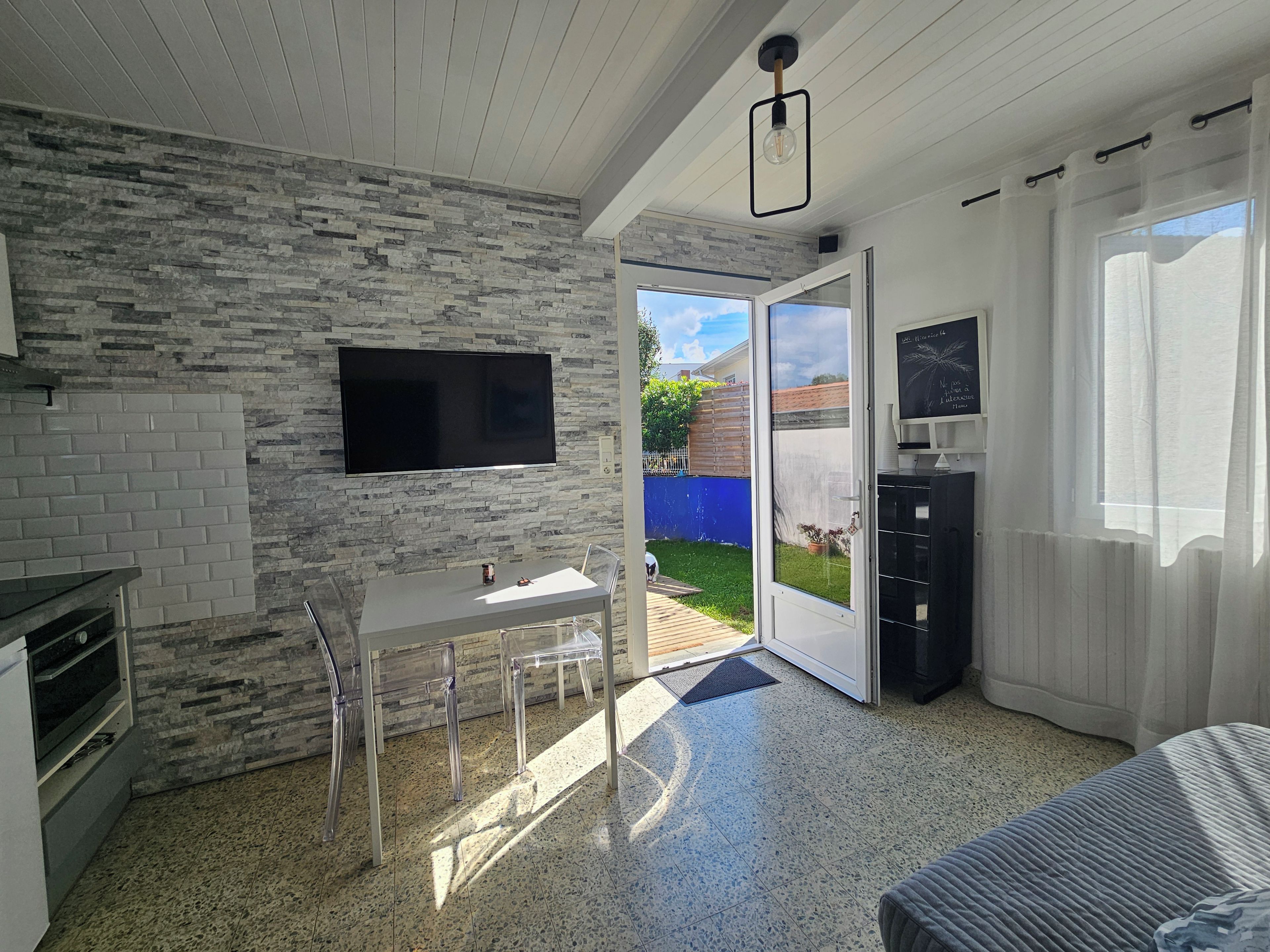 A modern kitchen with a stone backsplash, a flat-screen TV, and a dining area with a table and chairs.